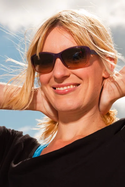 ビーチで幸せなかなり金髪女。自然を楽しんでいます。青い曇り空。黒いセーターとサングラスを着用. — ストック写真