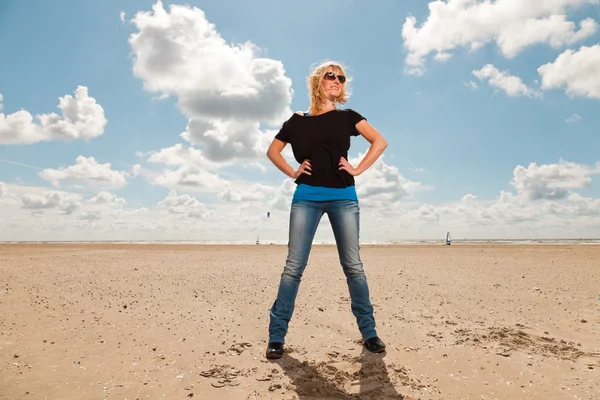 Счастливая блондинка на пляже. Наслаждаюсь природой. Голубое облачное небо. В черном свитере и солнечных очках . — стоковое фото