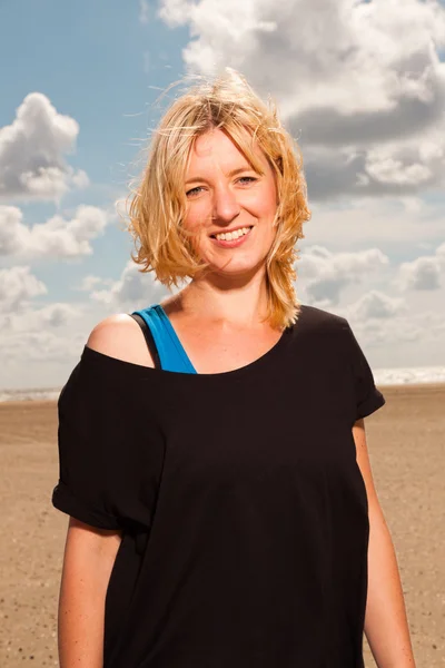 Glad ganska blond kvinna på stranden. njuter av naturen. blå mulen himmel. klädd i svart tröja. — Stockfoto
