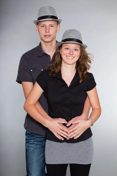 Happy young couple wearing a hat casual dressed. Studio shot isolated on grey background. Man with short blond hair. Woman long brown hair. — Stock Photo, Image