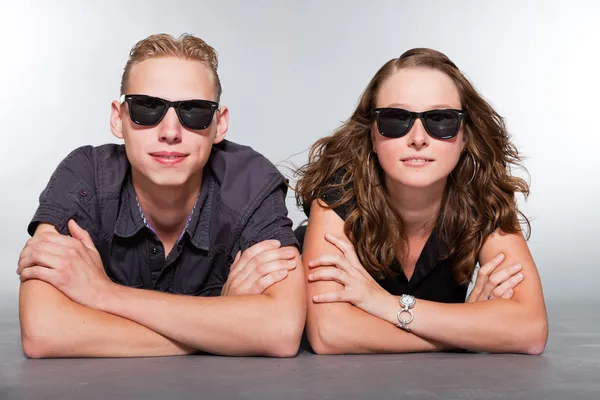 Happy young couple with black sunglasses casual dressed. Studio shot isolated on grey background. Man with short blond hair. Woman long brown hair. — Stock Photo, Image