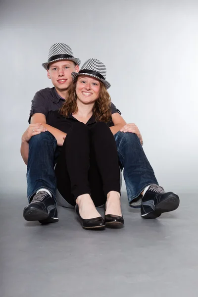 Lyckliga unga par som bär en hatt avslappnad klädd. Studio skott isolerade på grå bakgrund. man med kort blont hår. kvinna långa bruna hår. — Stockfoto