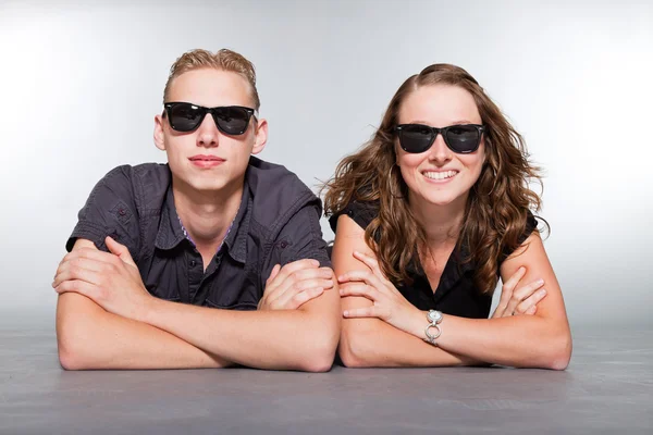 Happy young couple with black sunglasses casual dressed. Studio shot isolated on grey background. Man with short blond hair. Woman long brown hair. — Stock Photo, Image