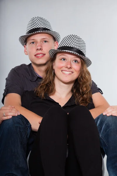 Gelukkige jonge paar dragen van een hoed casual gekleed. studio opname geïsoleerd op grijze achtergrond. man met kort blond haar. vrouw lang bruin haar. — Stockfoto