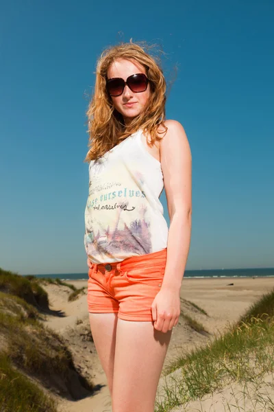 Boldog szép hosszú vörös hajú lány napszemüveg élvezi homokdűnék a strand közelében, a forró nyári napon. tiszta kék ég. — Stock Fotó
