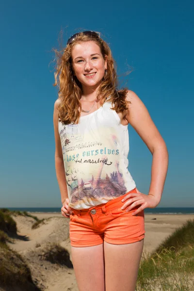 Glad söt flicka med långa röda hår njuter av sanddynerna nära stranden på varm sommardag. klar blå himmel. — Stockfoto