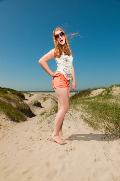 Happy pretty girl with long red hair and sunglasses enjoying sand dunes near the beach on hot summers day. Clear blue sky. — Stock Photo, Image