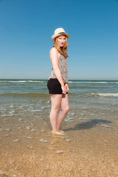 Ευτυχισμένο το όμορφο κορίτσι με μακριά κόκκινα μαλλιά και καπέλο απολαμβάνοντας δροσιστικά παραλία την ημέρα καλοκαίρια. σαφή μπλε ουρανό. — Φωτογραφία Αρχείου