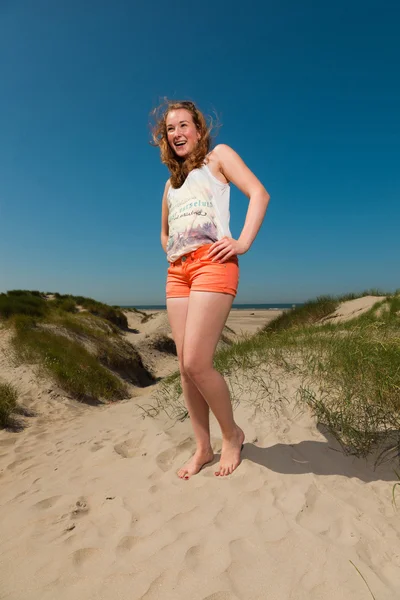 暑い夏の日に、ビーチ近くの砂丘を楽しんで長い赤髪と幸せなきれいな女の子。澄んだ青い空. — ストック写真