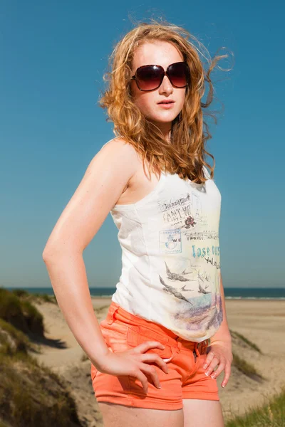 Felice bella ragazza con lunghi capelli rossi e occhiali da sole godendo di dune di sabbia vicino alla spiaggia nelle estati calde giorno. Cielo azzurro chiaro . — Foto Stock