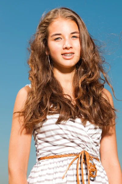 Счастливая красивая девушка с длинными каштановыми волосами наслаждается на открытом воздухе в жаркий летний день. Ясное голубое небо . — стоковое фото