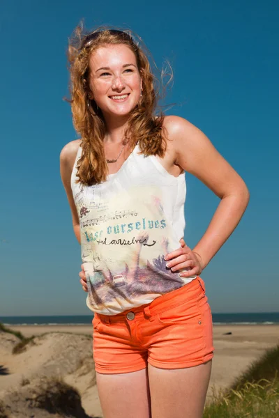 Menina bonita feliz com longos cabelos vermelhos desfrutando de dunas de areia perto da praia no dia quente de verão. Céu azul claro . — Fotografia de Stock