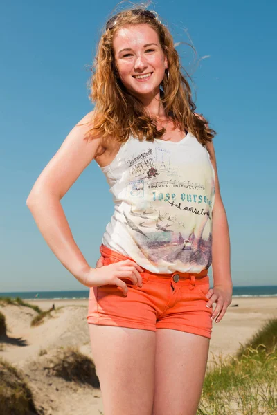 Šťastné hezká dívka s dlouhé červené vlasy písečných dun nedaleko pláže se těší horká léta den. modré nebe nad hlavou. — Stock fotografie