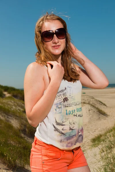 Glückliches hübsches Mädchen mit langen roten Haaren und Sonnenbrille, das an heißen Sommertagen Sanddünen in Strandnähe genießt. blauer Himmel. — Stockfoto