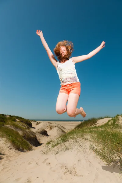 Happy pretty girl with long red hair enjoying sand dunes near the beach on hot summers day. Clear blue sky. — Stock Photo, Image