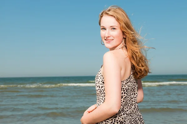 Glad söt flicka med långa röda hår njuta av uppfriskande stranden på varm sommardag. klar blå himmel. — Stockfoto