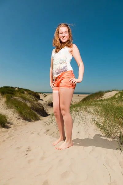 Menina bonita feliz com longos cabelos vermelhos desfrutando de dunas de areia perto da praia no dia quente de verão. Céu azul claro . — Fotografia de Stock