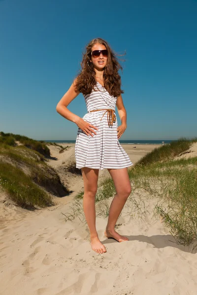 Menina bonita feliz com cabelos castanhos longos desfrutando de dunas de areia perto da praia no dia de verão quente. A usar monólogos. Céu azul claro . — Fotografia de Stock