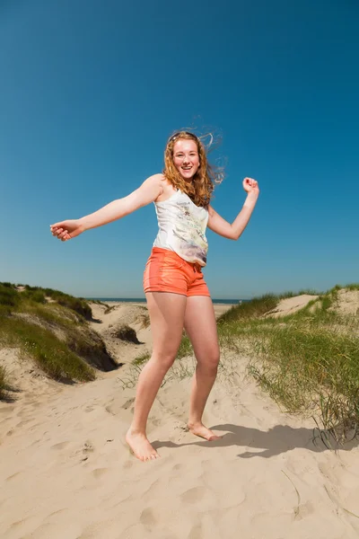 Happy pretty girl with long red hair enjoying sand dunes near the beach on hot summers day. Clear blue sky. — Stock Photo, Image