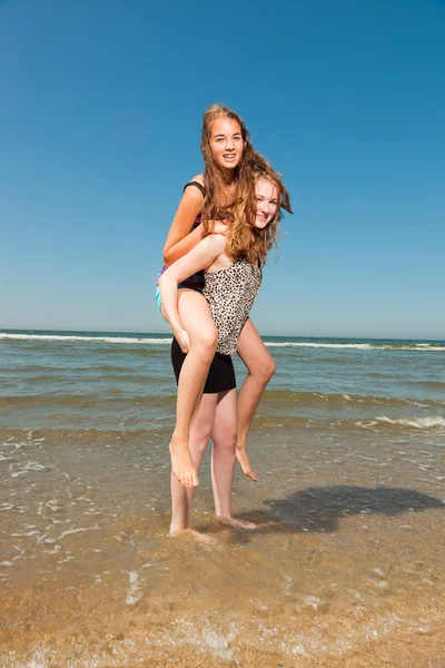 Dos chicas guapas jugando y disfrutando de lo refrescante en un caluroso día de verano. Cielo azul claro. Divertirse en la playa . — Foto de Stock
