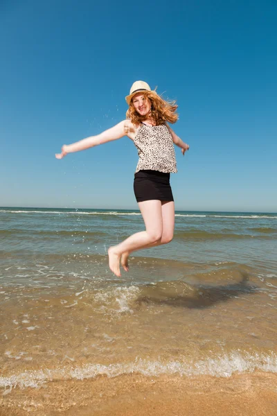 Feliz chica bonita con el pelo largo y rojo sombrero disfrutando de la playa refrescante en los veranos calurosos día. Cielo azul claro . —  Fotos de Stock