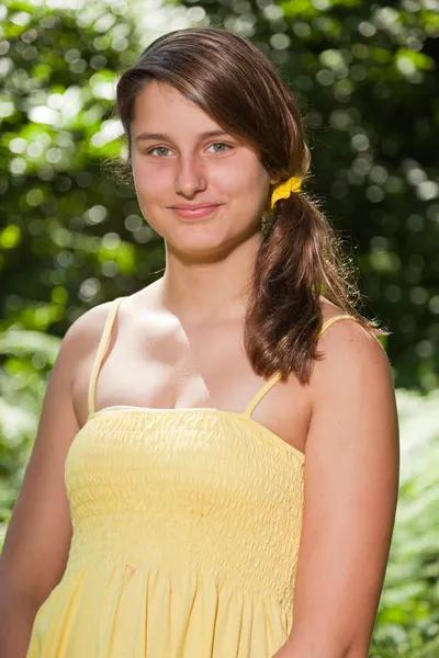 Pretty young woman with long brown hair enjoying nature in forest. Blurred green background. Wearing yellow dress. — Stock Photo, Image