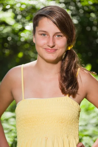 森林で自然を楽しんで長い茶色の髪とはかなり若い女性。緑の背景をぼかし。黄色のドレスを着ています。. — ストック写真