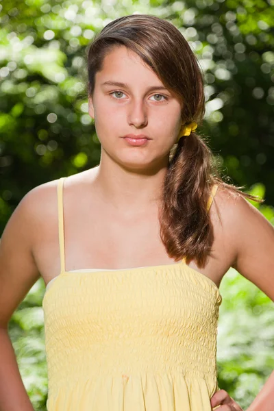 Hübsche junge Frau mit langen braunen Haaren, die die Natur im Wald genießt. verschwommener grüner Hintergrund. in gelbem Kleid. — Stockfoto