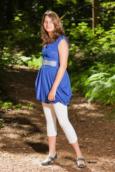 Mooie jonge vrouw met lang bruin haar genieten van natuur in het bos. groene gebladerte achtergrond. draagt blauwe jurk. — Stockfoto