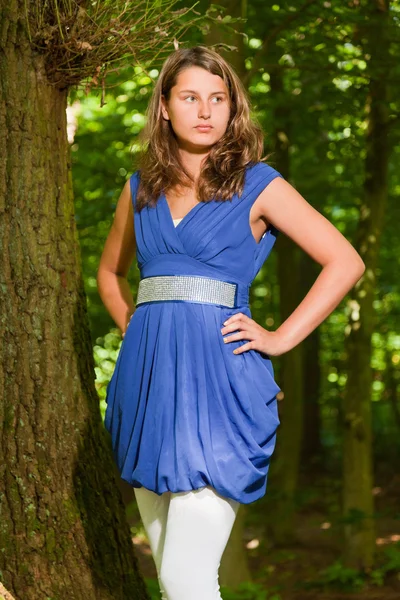 Ganska ung kvinna med långa bruna hår njuter av naturen i skogen. gröna blad bakgrund. klädd i blå klänning. — Stockfoto