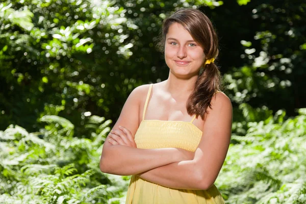 Hübsche junge Frau mit langen braunen Haaren, die die Natur im Wald genießt. verschwommener grüner Hintergrund. in gelbem Kleid. — Stockfoto