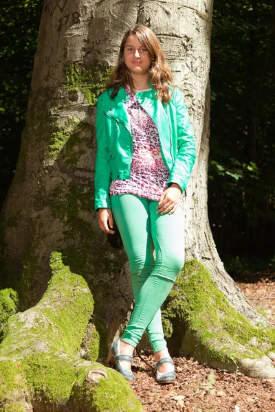Pretty young woman with long brown hair enjoying nature in forest. Foliage in background. Wearing green jacket and trousers. Cool looking. Tough girl. — Stock Photo, Image