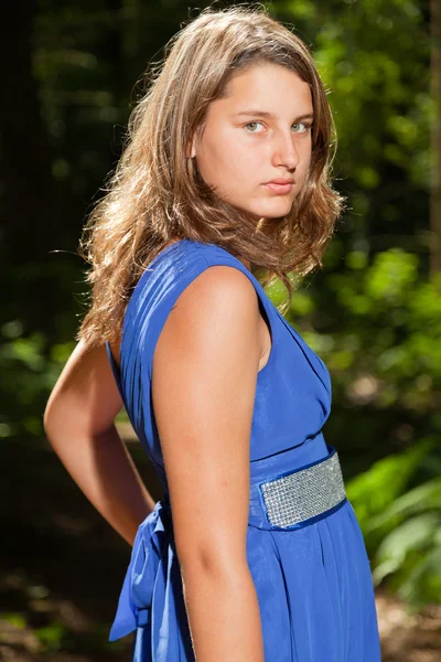 Jolie jeune femme aux longs cheveux bruns profitant de la nature en forêt. Feuillage vert. Porter une robe bleue . — Photo