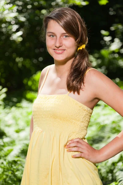 Ganska ung kvinna med långa bruna hår njuter av naturen i skogen. suddiga grön bakgrund. bär gula klänning. — Stockfoto