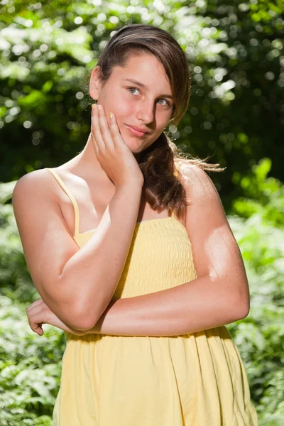 Csinos, fiatal nő, hosszú barna haja élvezi természet erdőben. homályos zöld háttér. sárga ruha viselése. — Stock Fotó