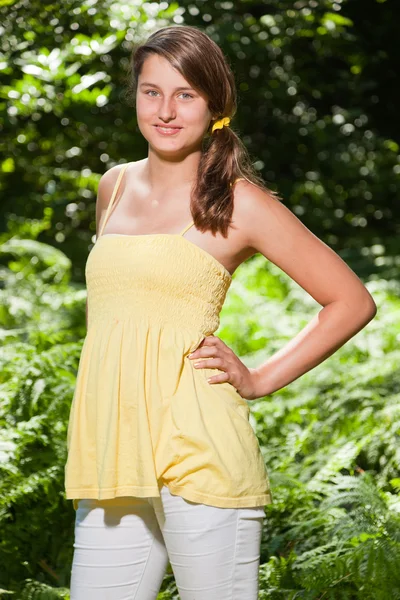 Mujer joven y bonita con cabello castaño largo disfrutando de la naturaleza en el bosque. Fondo verde borroso. Vestido amarillo . — Foto de Stock