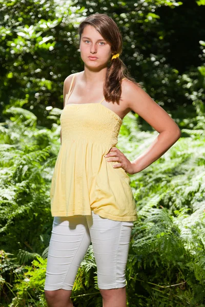 Mujer joven y bonita con cabello castaño largo disfrutando de la naturaleza en el bosque. Fondo verde borroso. Vestido amarillo . — Foto de Stock