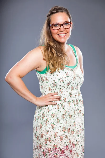 Pretty woman with long brown hair wearing glasses and flower dress. Fashion studio shot isolated on grey background. — Stock Photo, Image