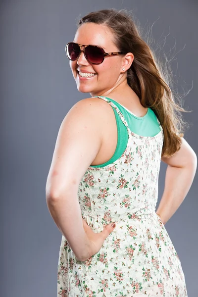 Pretty woman with long brown hair wearing sunglasses and flower dress. Fashion studio shot isolated on grey background. — Stock Photo, Image