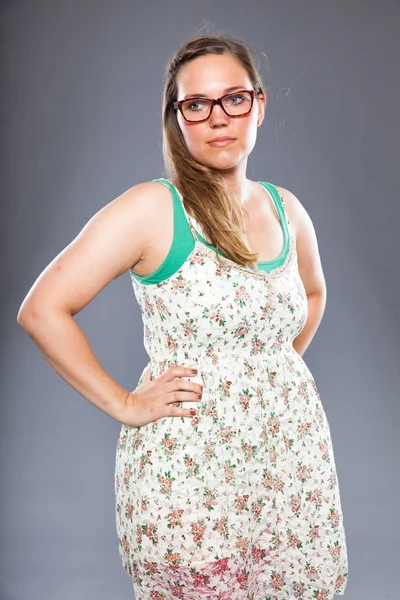 Pretty woman with long brown hair wearing glasses and flower dress. Fashion studio shot isolated on grey background. — Stock Photo, Image