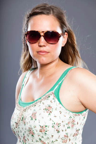 Mulher bonita com cabelo castanho longo usando óculos de sol e vestido de flor. Estúdio de moda tiro isolado em fundo cinza . — Fotografia de Stock