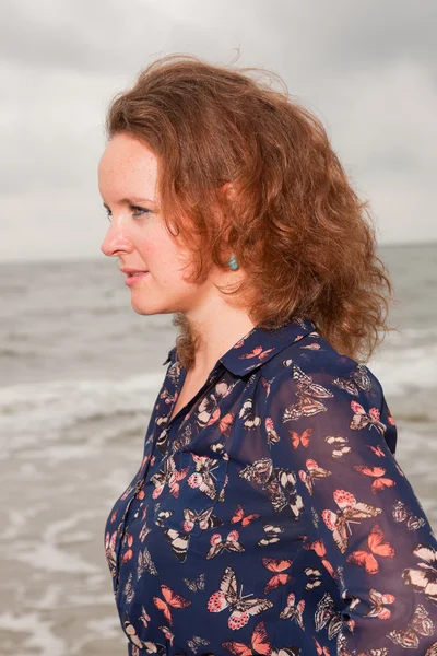 Csinos, fiatal nő élvezi a kültéri jellegét, a strand közelében. vörös hajú. sötét kék ruhát visel. felhős ég. — Stock Fotó