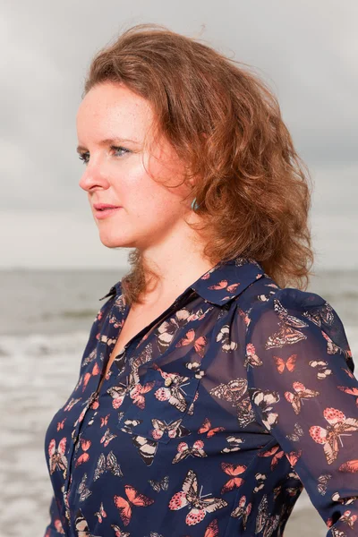 Hübsche junge Frau, die die Natur in Strandnähe genießt. rote Haare. trägt ein dunkelblaues Kleid. Bewölkter Himmel. — Stockfoto