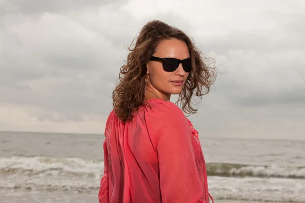 해변 근처 야외 자연 즐기는 행복 한 젊은 여자. 갈색 머리입니다. 핑크 셔츠와 블랙 선글라스를 착용. 흐린 하늘. — 스톡 사진
