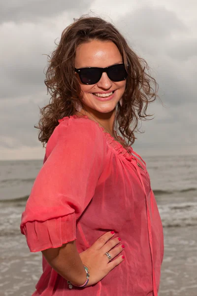 Boldog fiatal nő élvezi a kültéri jellegét, a strand közelében. barna haj. viselt, rózsaszín inget és fekete napszemüveg. felhős ég. — Stock Fotó