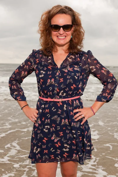 Jolie jeune femme appréciant la nature en plein air près de la plage. Cheveux roux. Elle porte une robe bleu foncé. Ciel nuageux . — Photo