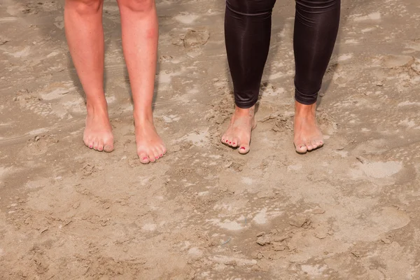 两个年轻的女子站在海滩上的沙子的脚. — 图库照片