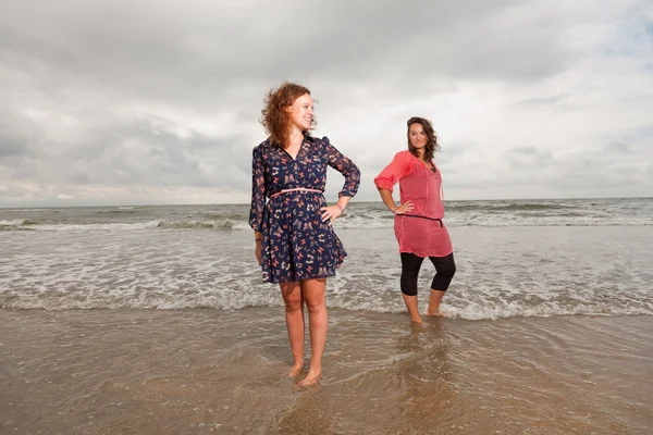 Två glada tjejer njuta utomhus natur nära stranden. röda och bruna hår. molnig himmel. — Stockfoto