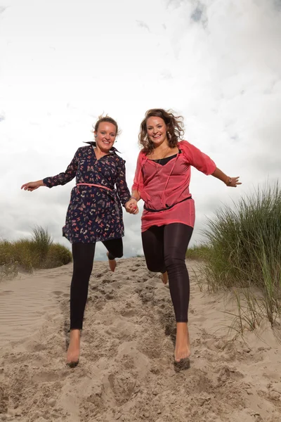 Két boldog lányok élvezik a szabadtéri jellegét, a strand közelében. Ugrás a levegőben. vörös és barna haj. felhős ég. — Stock Fotó