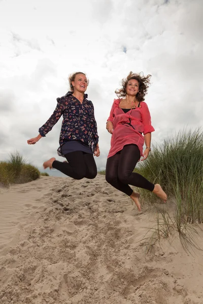 Dwa szczęśliwy dziewczyny świeżym z przyrodą w pobliżu plaży. skoki w powietrzu. czerwone i brązowe włosy. pochmurnego nieba. — Zdjęcie stockowe
